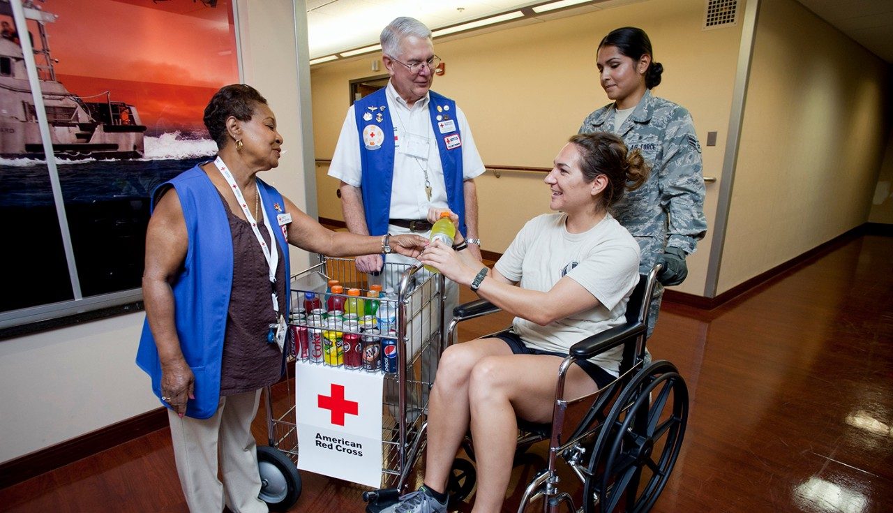 woman in wheelchair assisted by military personnel