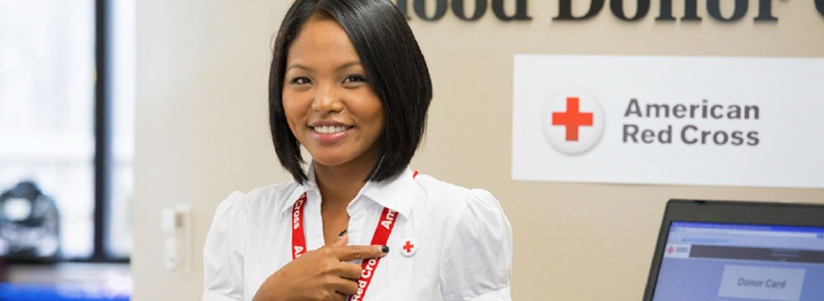 woman pointing to red cross pin on shirt