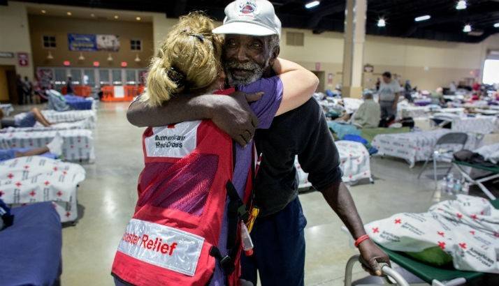 A Red Cross volunteer hugs a man in a shelter.