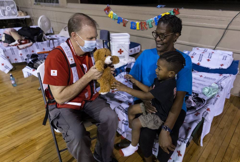 Red Cross volunteer gives a teddy bear to a young boy in a Red Cross shelter