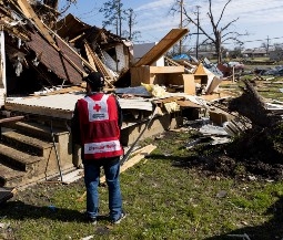 red cross volunteer standing near destroyed house