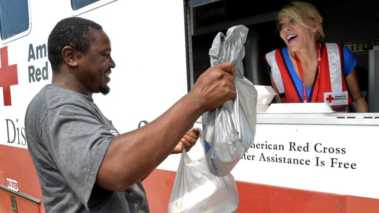 Red Cross volunteer in Red Cross vehicle handing packaged food to man